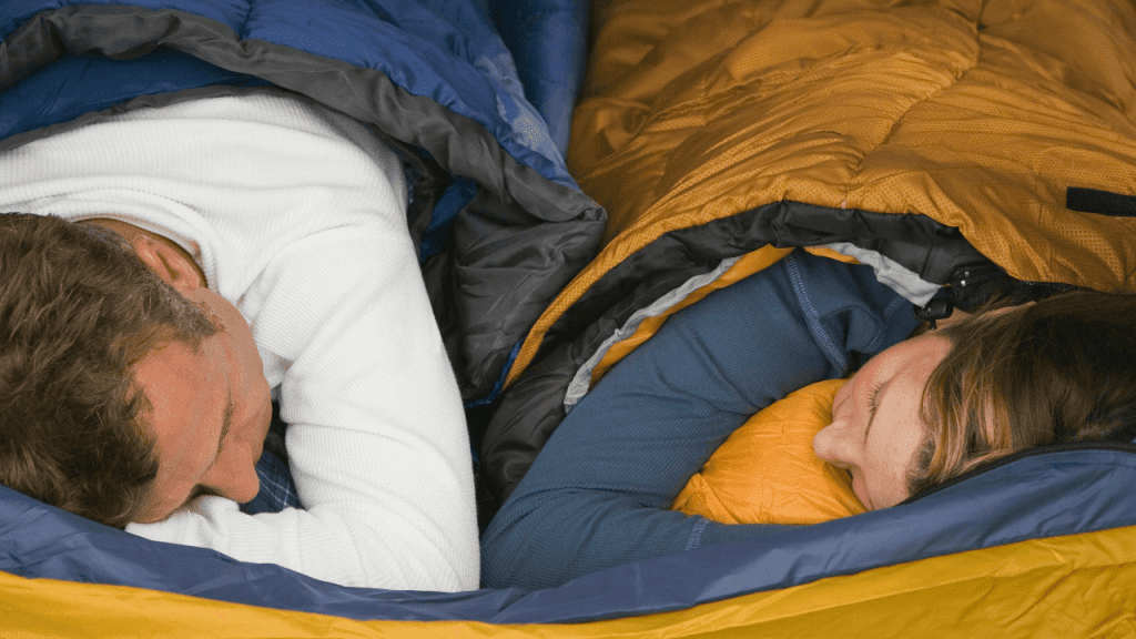 Man and woman sleeping comfortably in sleeping bags while camping.