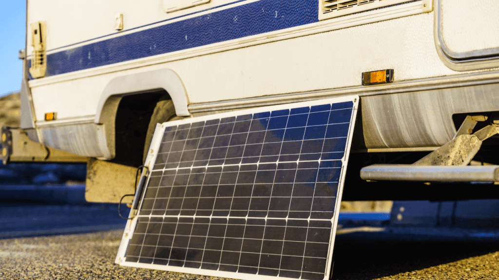 Portable solar panels set up on the ground next to a caravan at a sunny campsite, capturing sunlight to provide clean, renewable energy for powering the caravan’s electrical needs.