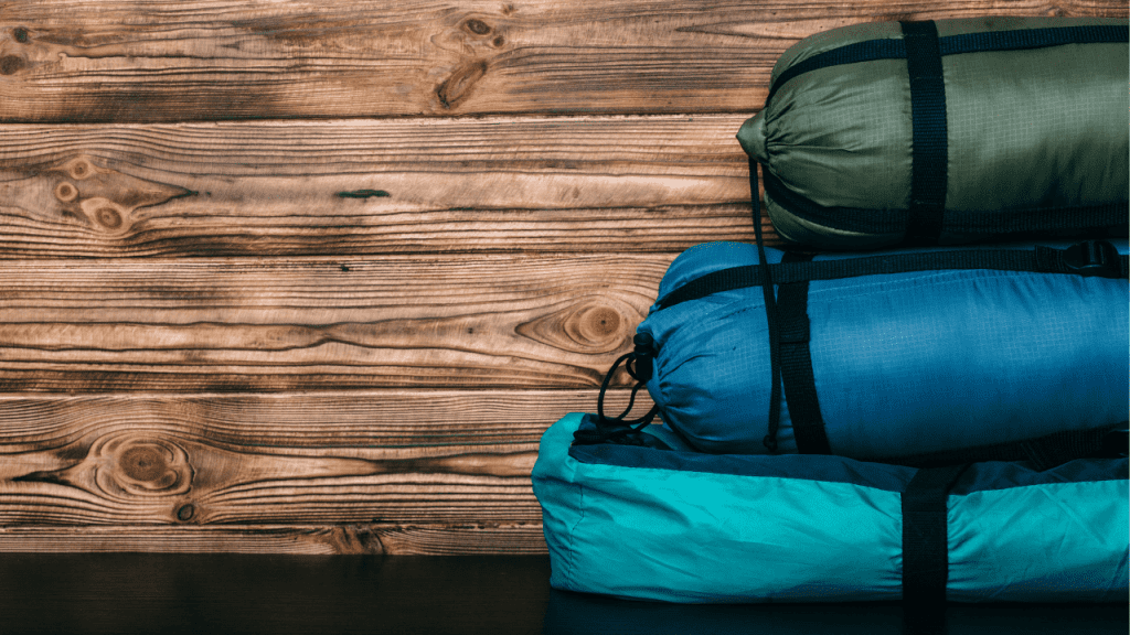 Three rolled up tents of different shades of blue and of different sizes stacked up on one another.