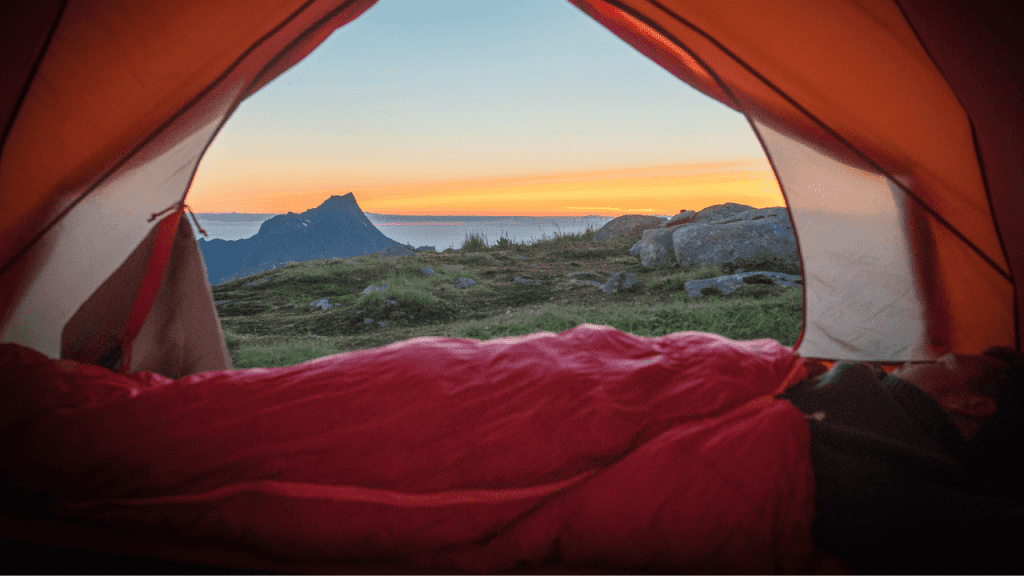 View of the mountains and horizon from the inside of a tent with a man inside his sleeping bag.