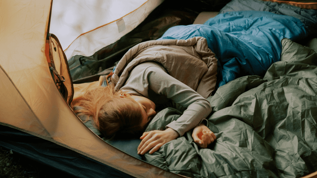 Woman asleep comfortably in her sleeping bag inside her tent while camping.