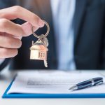 A licensed Buyers Agent offers a house key over a signed contract, representing the decision to sell or rent your home to travel Australia and stay invested in the Australian property market.