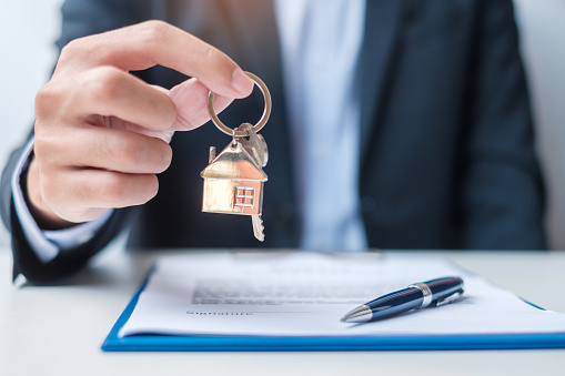 A licensed Buyers Agent offers a house key over a signed contract, representing the decision to sell or rent your home to travel Australia and stay invested in the Australian property market.