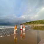ravelers standing on the shore of Agnes Water beach in Queensland, with storm clouds over the ocean and a lush green headland in the background.