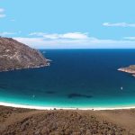 Aerial view of Wineglass Bay in Freycinet National Park, Tasmania, featuring a curved white sand beach and turquoise water.